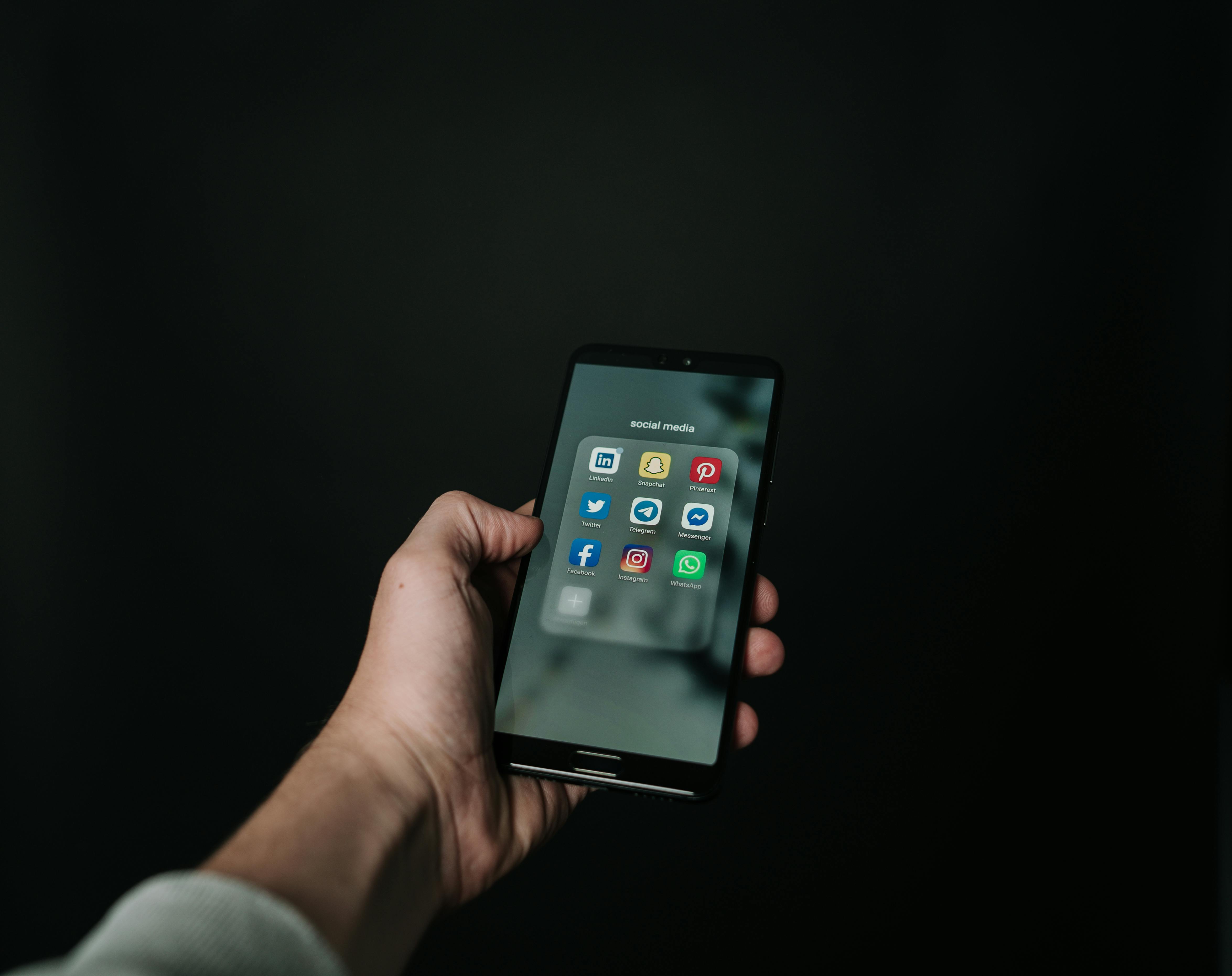 Smartphone mostrando carpeta de apps de comunicación: WhatsApp, Instagram, Telegram, Messenger, LinkedIn y más